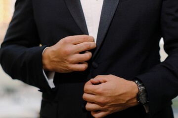 Obraz premium Close-up of a man adjusting his suit jacket, with a focus on his hands and a wristwatch.