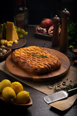 Cheese pastry pie on a dark table among products, oils, vegetables and fruits