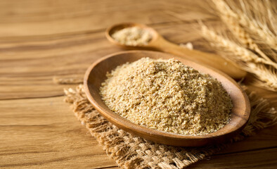 pile of flake whole grain powder or wheat germ in wood bowl and spoon on wooden table rustic style background with copy space