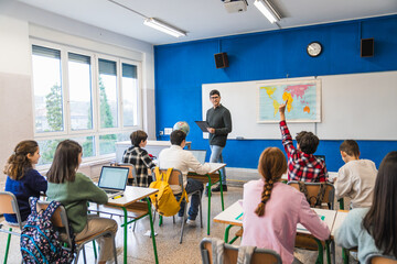Students raising hand in geography class with teacher explaining lesson