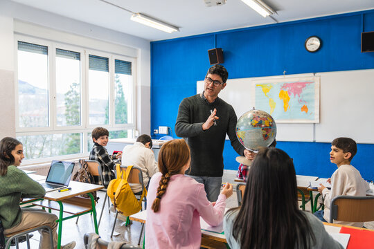 Geography teacher explaining lesson using globe in classroom