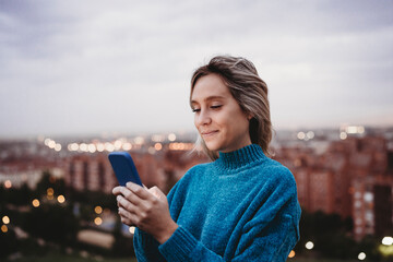Smiling woman text messaging through smart phone at dusk