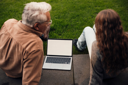Grandfather giving advice to granddaughter outdoors with a laptop