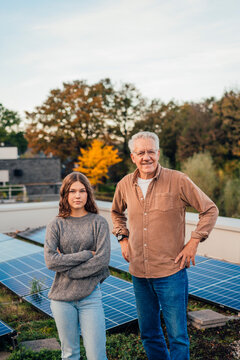 Grandfather and granddaughter standing by solar panels outdoors