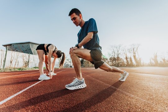 Man and a woman stretching on a sunny outdoor track, preparing for exercise