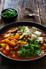 Fresh vegetable soup with chickpeas, feta cheese and cilantro on wooden table