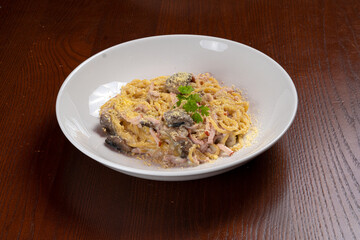 Spaghetti with cheese sauce and ham in white plate on wood background