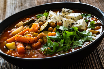 Fresh vegetable soup with chickpeas, feta cheese and cilantro on wooden table