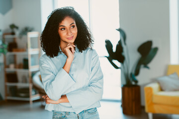 Young woman with confident expression posing in a cozy, well lit living space adorned with greenery and bright decor