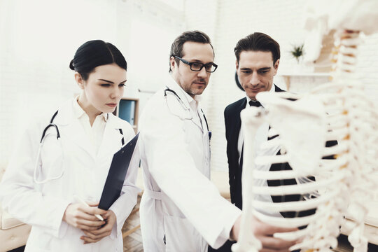 Physiotherapist shows problem zone of ribs on anatomical model to patient in medical office.