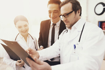 Fototapeta premium Experienced doctor with nurse shows results of analyzes to smiling businessman in office.