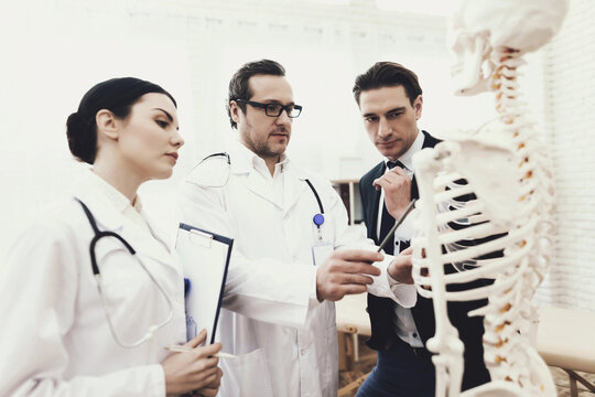 Physiotherapist shows problem zone of ribs on anatomical model to patient in medical office. - Powered by Adobe