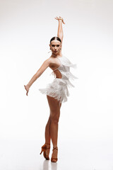 Elegant female dancer in a dynamic Latin pose, wearing a white fringe dress and high heels, exuding...