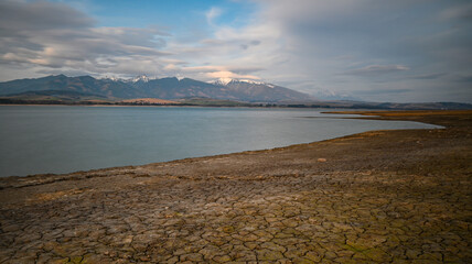 Dry cracked earth near Liptovska Mara with snow capped mountains in the background, highlighting...