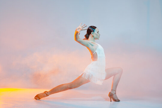 Dynamic dance solo. Woman dancing bachata on gradient yellow-orange background in neon light. Dance concept, lessons, school