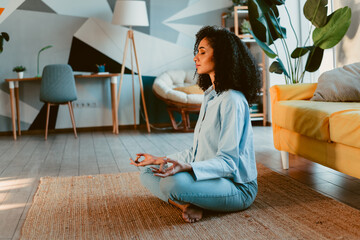 Young woman meditating on a rug in a stylish living room with modern decor and sunlight enhancing...