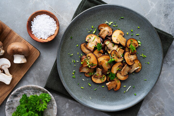 Fried brown mushroom slices in a dish, paired with raw champignons.