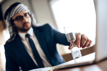 Arab businessman with hourglass at table at hotel room.