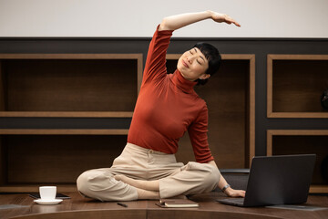 Peaceful Japanese woman sitting on desk in the office and doing yoga relaxation exercises.