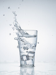 Ice cubes falling with splashes into glass water on light blue background.