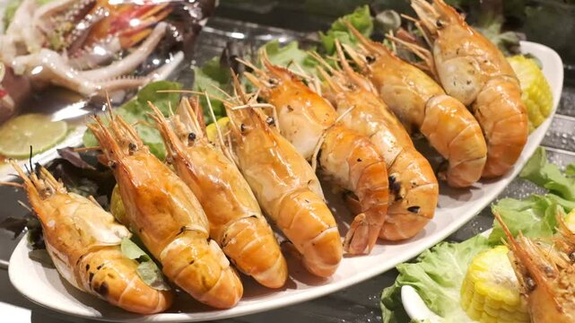 A plate of shrimp is on a table with a green salad. The shrimp are arranged in a row and are garnished with lemon wedges