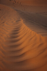 Views of the Dubai desert at sunset, footprints in the sand, with wind sweeping grains off the dunes.