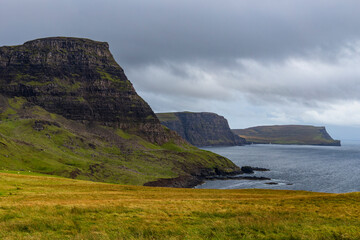 Neist Point at sunset is a breathtaking sight—its lighthouse stands against dramatic cliffs, with waves crashing below. A rainbow arches over the ocean, painting the rugged Isle of Skye magical light