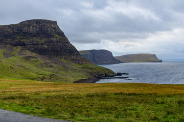 Neist Point at sunset is a breathtaking sight&mdash;its lighthouse stands against dramatic cliffs, with waves crashing below. A rainbow arches over the ocean, painting the rugged Isle of Skye magical light