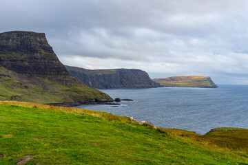 Neist Point at sunset is a breathtaking sight&mdash;its lighthouse stands against dramatic cliffs, with waves crashing below. A rainbow arches over the ocean, painting the rugged Isle of Skye magical light