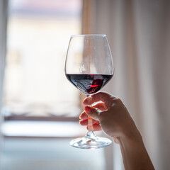 Female hand holding a glass of red wine in front of the window