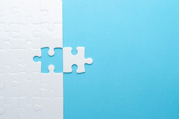 Concept for problem-solving, teamwork, solutions, or missing connections. White jigsaw puzzle on a vibrant blue background with one missing piece. Minimalist composition with copy space.