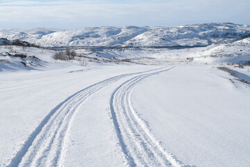 Obraz premium Car tracks on an abandoned road to Zavalishina Bay on a sunny March day. The surroundings of the village of Teriberka. Murmansk region, Russia