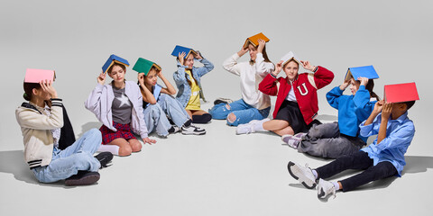 Group of students sit in circle with books balanced on heads, looking up, representing fun and...