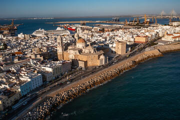 Fototapeta premium Aerial view of Cadiz Cathedral with its golden dome glowing in sunlight, surrounded by whitewashed buildings and a bustling port along the Atlantic coast