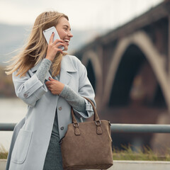 Young woman in blue coat talking phone. Autumn city background.