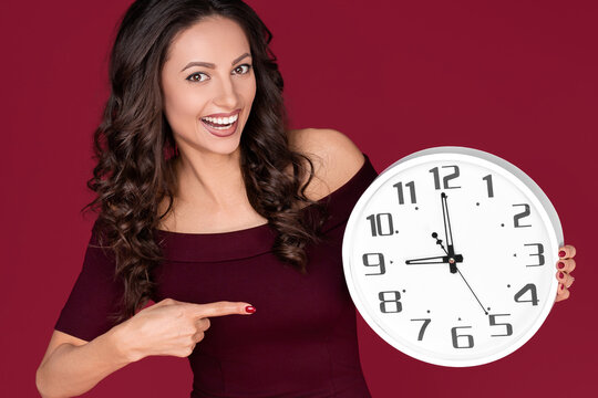 Happy young modern business woman in maroon dress point finger on clock