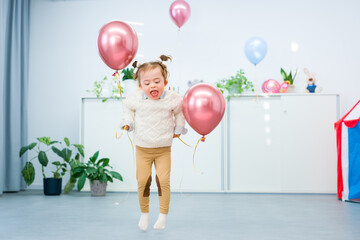 Cute 3 year old girl with Down Syndrome celebrating her birthday in a playroom decorated with balloons. Kids birthday party.