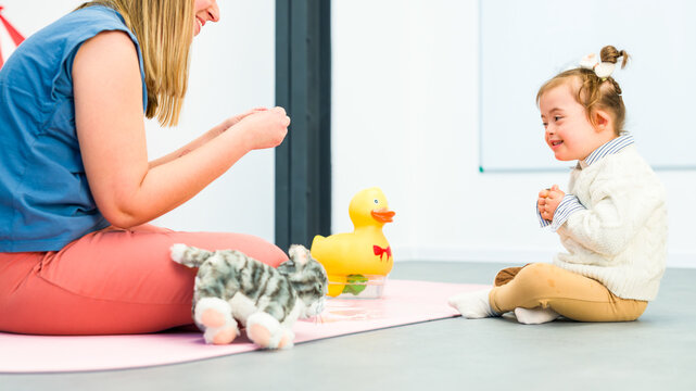 Nonverbal child with Down syndrome learning baby sign language with the help of a speech therapist. Child therapy, neurodiversity, learning difficulty, developmental disability.