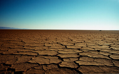 Vast cracked earth stretches to meet a clear blue sky at the horizon.  Dry, barren landscape under the sun, showing parched ground and arid conditions.