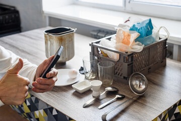 Man with smartphone reading recipe for making delicious home bread, baking ingredients and kitchenware on the background. Home bread baking with smartphone recipe, flour, and dough on kitchen table