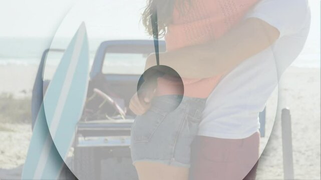By beach, couple embracing with surfboard and truck in background