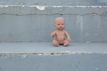 Naked plastic baby doll sitting alone on worn concrete steps with peeling paint, creating a feeling of abandonment and contrast between childhood and urban decay