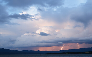 Dramatic storm clouds fill the sky with flashes of lightning illuminating distant mountains above a body of water.