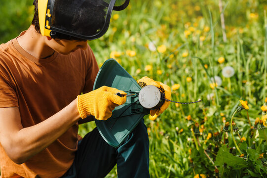 A young worker attaches a protective shield to an electric grass trimmer by screwdriver. Safety and protection when working with an electric scythe.