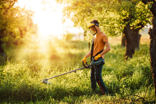 Mowing grass with an electric lawn trimmer. Young man mowing grass in the garden or park. Spring work in the garden.