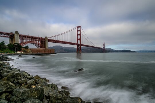 Golden Gate Bridge in San Francisco with a dramatic cloudy sky and rocky shoreline - Powered by Adobe