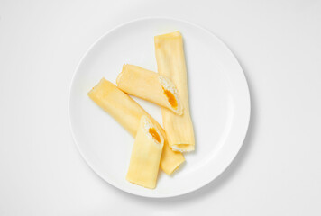 Crepe roll with cottage cheese and mango jam on a white plate, viewed from above on a white background