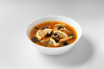 Solyanka soup served on a white plate against a white background, top view