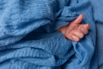 Gentle baby hand emerging from soft blue fabric