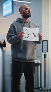 Transportation Service in International Airport Terminal: Airport Greeters Holding Name Sign, Waiting for Passengers From Plane Flight. Diverse People and Travelers Walking with Luggage. Vertical Shot